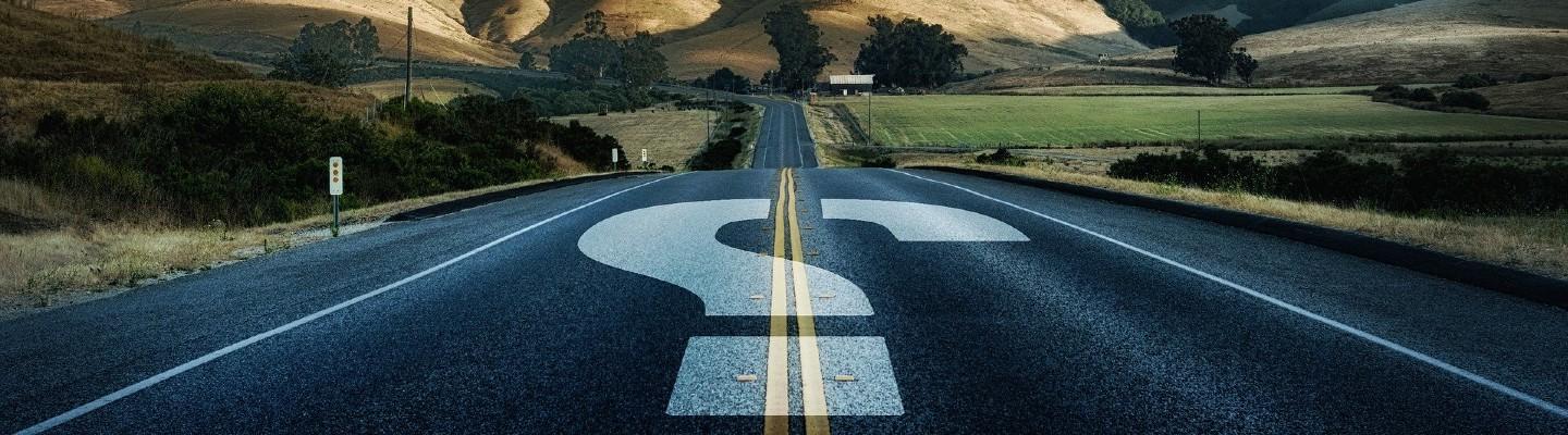 A road heading into the mountains with a big white question mark on it